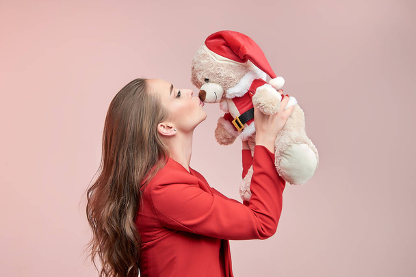 Joven mujer hermosa con el pelo ondulado largo besa a un oso de juguete a la imagen de Santa Claus. Concepto de Año Nuevo. - Foto, imagen