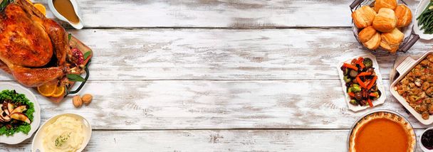 Traditioneel Thanksgiving kalkoen diner. Bovenaanzicht dubbele rand op een rustieke witte houten banner achtergrond met kopieerruimte. Turkije, aardappelpuree, dressing, pompoentaart en kant en klaar. - Foto, afbeelding