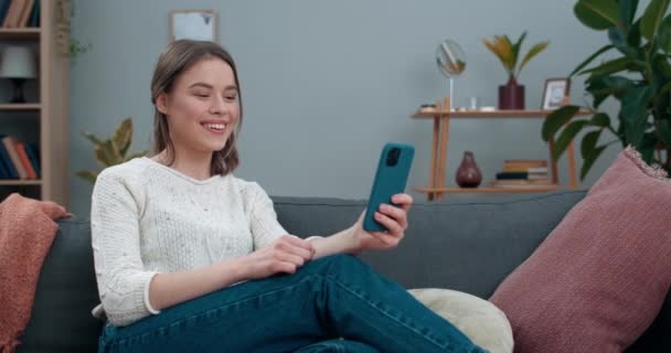 Süket Y-generációs nő videóhívással és jelbeszéddel, finom hírekkel, miközben a kanapén ül. A nő mosolyog, miközben az okostelefont használja kommunikációra. Hallásvesztés. - Felvétel, videó