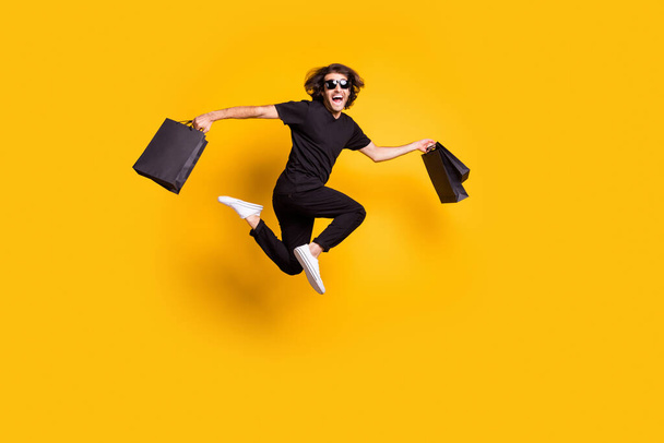 Full length body size portrait of man jumping up keeping packages after sale on black friday isolated on bright yellow color background - Zdjęcie, obraz