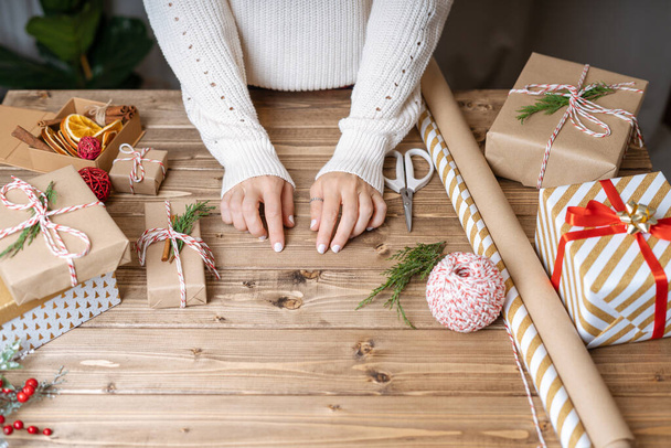 Vrouwen handen inpakken kerstcadeau, sluiten. Onvoorbereide geschenken op houten ondergrond met decorelementen en voorwerpen, bovenaanzicht. Kerst of Nieuwjaar DIY verpakking Concept. Stap voor stap - Foto, afbeelding