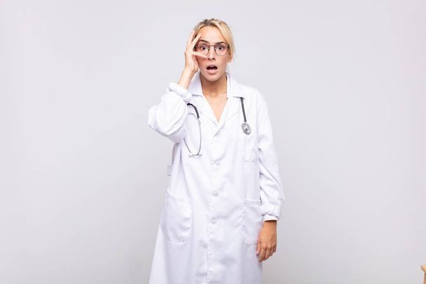 young woman physician looking shocked, scared or terrified, covering face with hand and peeking between fingers - Foto, Imagem