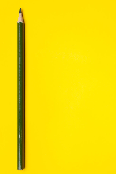 vertical dark green sharp wooden pencil on a bright yellow background, isolated, copy space, mock up - Photo, Image