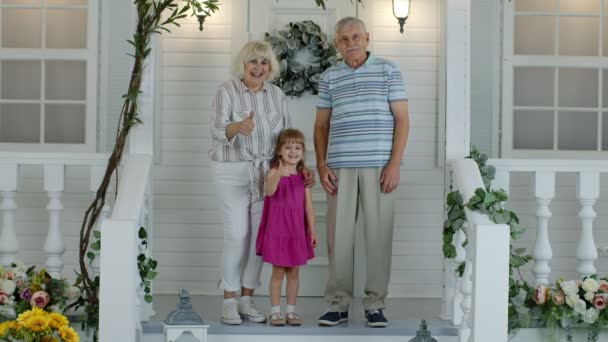 Ηλικιωμένοι παππούδες ζευγάρι με εγγονή στη βεράντα στο σπίτι κουνώντας το χέρι, δείχνοντας τους αντίχειρες επάνω - Πλάνα, βίντεο