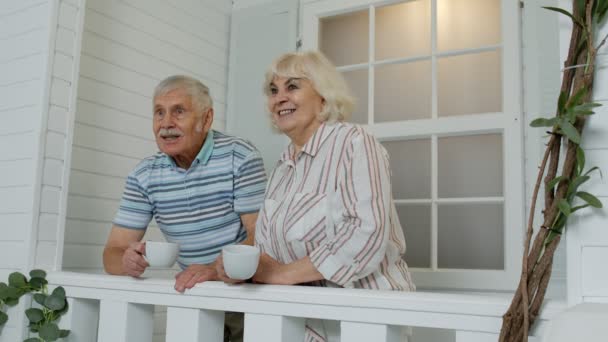 Anziani anziani coppia bere caffè, abbracciando in veranda a casa durante la quarantena coronavirus - Filmati, video