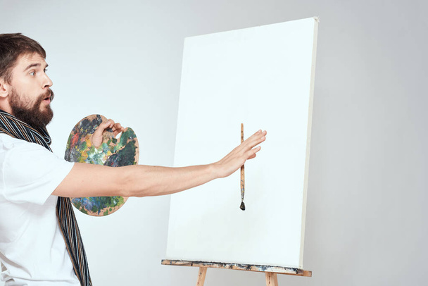 Male artist paints on easel palette art creativity light background - Foto, Imagem