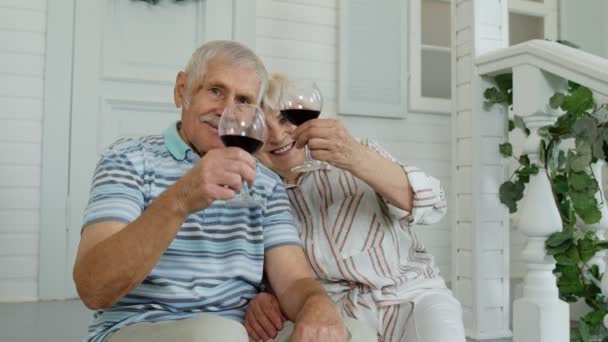 Aantrekkelijke oudere blanke echtpaar zit en drinkt wijn in de veranda thuis, het maken van een kus - Video