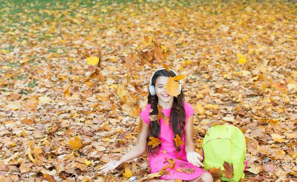 I would stay here forever. back to school. concept of online education. child sit in autumn leaves. girl in earphones with school bag. kid listen music in autumn park. fall is a time for study - Foto, immagini