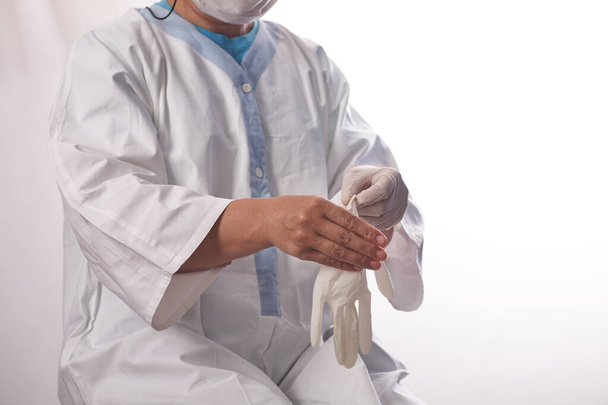 Proteger a los trabajadores sanitarios de la infección. Una doctora se pone guantes médicos sobre un fondo blanco aislado y sonríe. Equipos de protección individual antes del examen de los pacientes - Foto, imagen