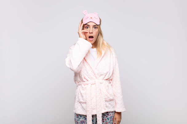 young pretty woman wearing pajamas, looking shocked, scared or terrified, covering face with hand and peeking between fingers - Photo, image