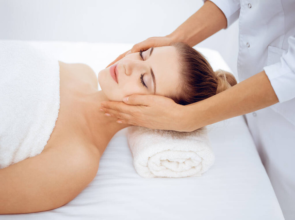 Young and blonde woman enjoying facial massage in spa salon. Beauty concept - Photo, image