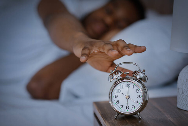 Ο κοιμισμένος Αφρικανός κλείνει το ξυπνητήρι ξυπνώντας στο σπίτι. - Φωτογραφία, εικόνα