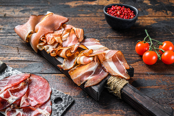 Meat antipasto board, pancetta, salami, sliced ham, sausage, prosciutto, bacon. Dark Wooden background. Top view. - Foto, afbeelding