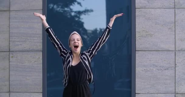 Junge attraktive Studentin Modell steht auf der Straße vor der Kamera fühlt Freude Triumph laut schreit vor Glück hebt die Hände siegreich springen in die Luft, Erfolgsfeier Konzept - Filmmaterial, Video