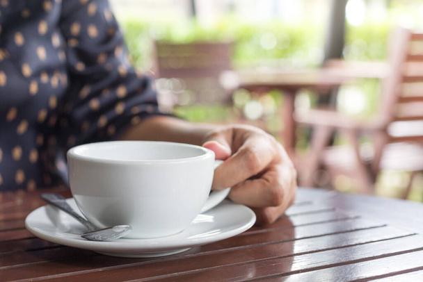Ręka kobiety trzyma biały kubek kawy w kawiarni zamazane tło z porannym słońcem - Zdjęcie, obraz
