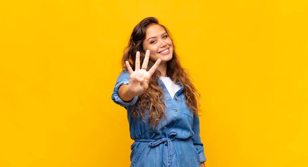 Woman smiling and looking friendly, showing number four or fourth with hand forward, counting down - Foto, afbeelding