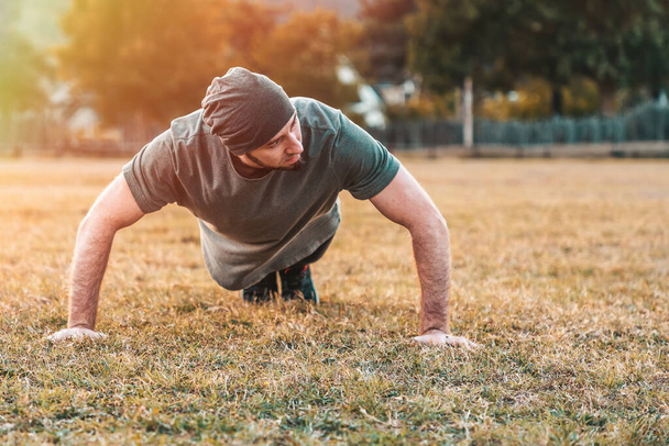 Sports and yoga. A man in sportswear push-ups during training. Park and trees on the background. Copy space. - Фото, зображення