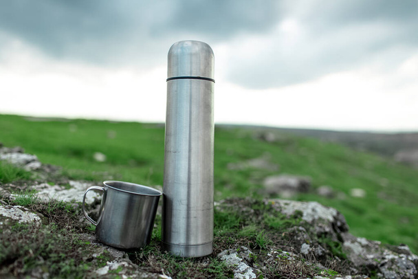 Close-up de aço inoxidável garrafa térmica e copo em pedra no campo verde. - Foto, Imagem