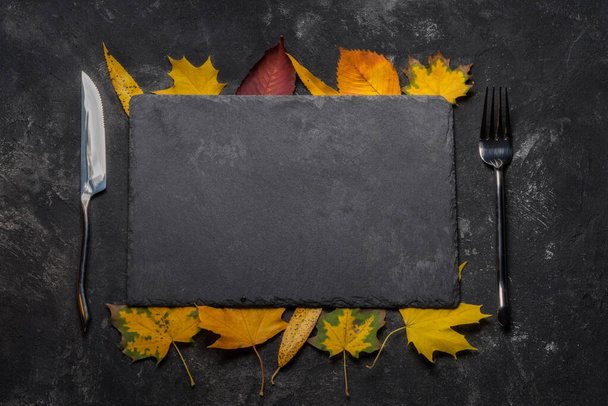 Herbstliches Layout mit Stillleben aus schwarzem Steintablett, Herbstblättern, Gabel und Messer. Herbst, Draufsicht. - Foto, Bild