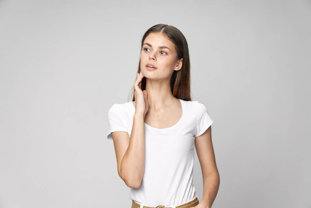 Uma mulher com uma t-shirt branca segura uma mão perto do rosto, um olhar para o lado  - Foto, Imagem