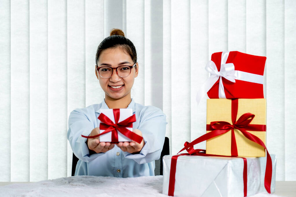 Woman in a blue shirt holding a white gift box tied with a red ribbon present for the festival of giving special holidays like Christmas, Valentine's Day. - Zdjęcie, obraz