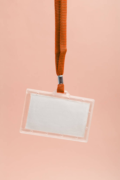 Insignia de plástico de negocios en blanco colgante con correa de cuello naranja contra fondo rosado  - Foto, imagen