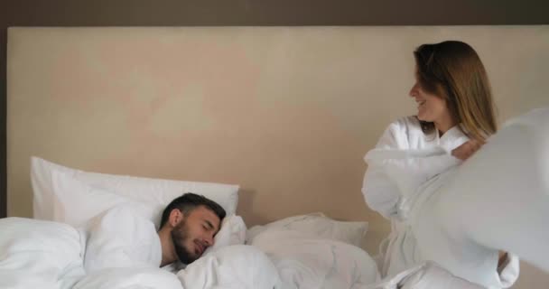Pareja tiene pelea de almohadas en cama cómoda en habitación de hotel - Metraje, vídeo