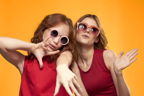 Happy sisters in red dresses on a yellow background are having fun and gesticulating Copy Space - Фото, изображение