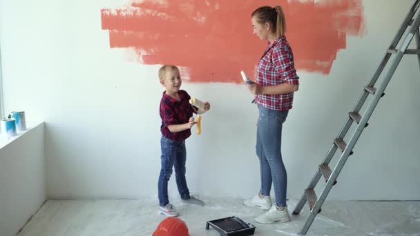 Anya és fia a fal mellett állnak egy narancssárga folttal. Üssétek egymást tenyéren. - Felvétel, videó