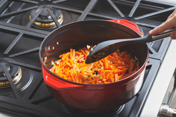 Keittäminen porkkana ja valkoinen sipuli hienonnettu ja kaadetaan punainen valurauta ranskalainen uuni - Valokuva, kuva