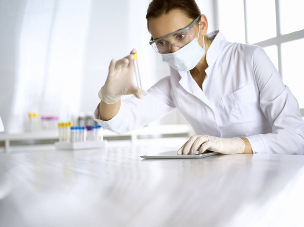 Female laboratory assistant analyzing a blood sample at hospital. Medicine, health care and researching concept - Foto, Bild