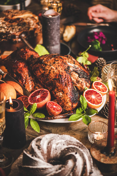 Family or friends celebrating Christmas or New Year. Holiday rustic wooden table with roasted turkey, chocolate cake, champagne and candles, red brick wall at background - Fotografie, Obrázek