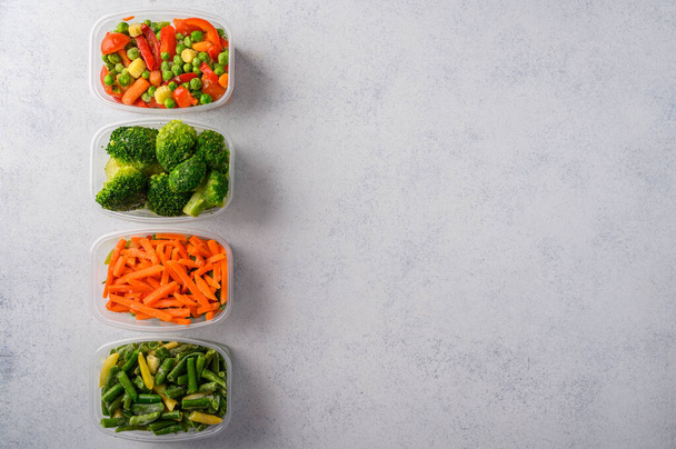 Frozen vegetables mix carrot, broccoli, green pods beans in plastic trays on light background, top view - Foto, Imagem