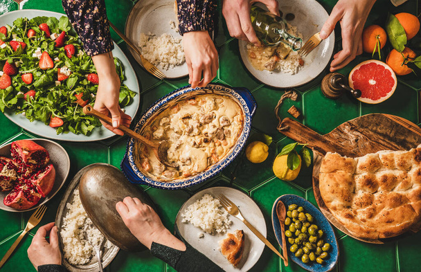 Perhe syö turkkilaista ruokaa. Tasainen-lay ihmiset kädet palvelevat ja syövät lampaan kanssa jogurtti kastike, tuoretta rucola ja mansikka salaatti, riisi pilav ja litteä leipä, ylhäältä. Ramazan iftar illallinen - Valokuva, kuva