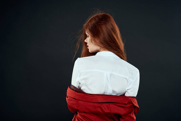 Vrouw in rood jasje wit shirt achteraanzicht donker achtergrond - Foto, afbeelding