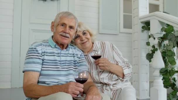 Pareja de ancianos mayores bebiendo vino, abrazándose en el porche en casa durante la cuarentena del coronavirus - Imágenes, Vídeo