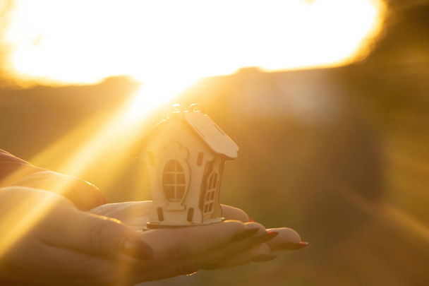 mains tenir une petite maison en bois sur le fond du soleil au coucher du soleil, maison de rêve - Photo, image