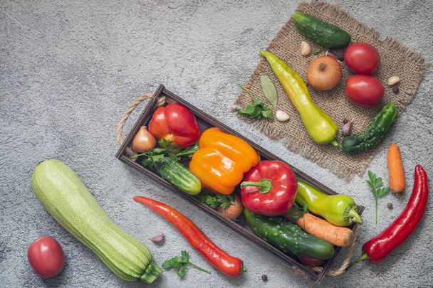 In a wooden container and on a napkin a variety of ripe vegetables: tomatoes, peppers, cucumbers, parsley, zucchini. Top view with copy space. Flat lay - Photo, Image