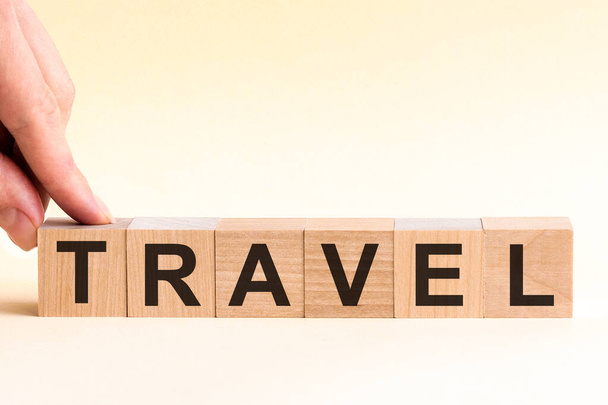 The hand puts a wooden cube with the letter T from the word TRAVEL. The word is written on wooden cubes standing on the yellow surface of the table. - Photo, Image