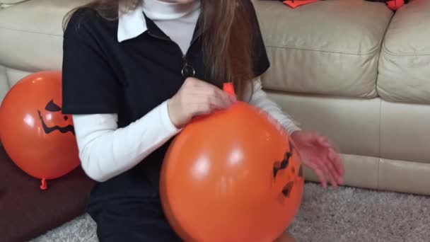 Dívka nafoukne oranžový hallowenový balón a uváže ho. Děti zdobí svůj domov na oslavu Halloweenu doma - Záběry, video