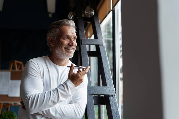 Casual Grey-haired Mature businessman talking on a mobile phone standing by the window. - Zdjęcie, obraz