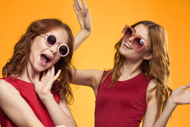 Mulher feliz e menina em vestido vermelho estão se divertindo em um fundo amarelo emoções da moda irmãs diversão espaço de cópia. - Foto, Imagem
