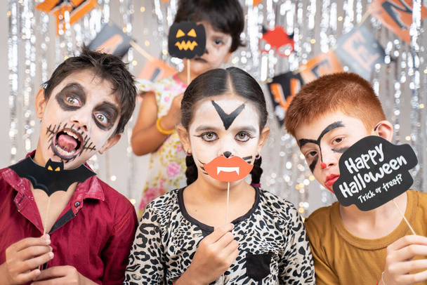 Группа детей в костюмах на Хэллоуин делает жестикулирующие страшные или жуткие лица, держа буфет на украшенном фоне, глядя в камеру. - Фото, изображение