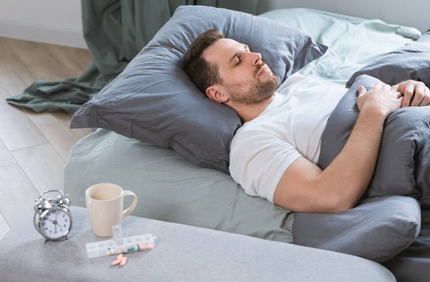 Ο άνθρωπος κοιμάται στο κρεβάτι μετά τη λήψη υπνωτικά χάπια στην κρεβατοκάμαρα - Φωτογραφία, εικόνα