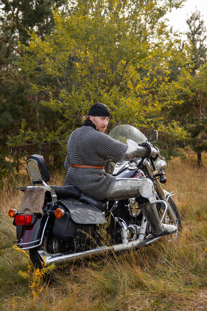 A biker in medieval knight's armor sits on a motorcycle against the background of the forest. - Photo, Image