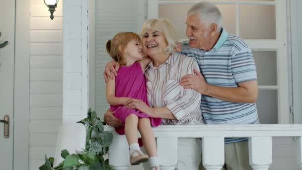 Nonno anziano e bambina abbracciano la nonna e fanno un bacio in veranda a casa - Filmati, video