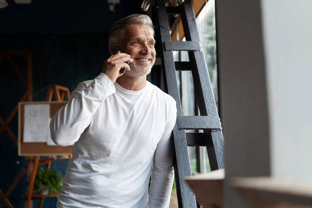 Случайно седой пожилой бизнесмен разговаривает по мобильному телефону у окна. - Фото, изображение