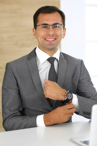 Cheerful smiling businessman sitting at a desk in modern office. Headshot of male entrepreneur or company director at workplace. Business concept - Photo, image
