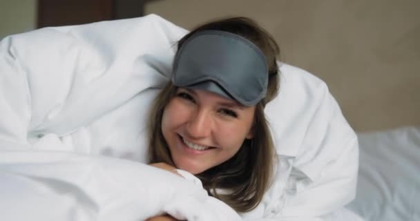 Συναισθηματική κυρία με μάσκα ύπνου και μαλακό πάπλωμα βρίσκεται στο κρεβάτι - Πλάνα, βίντεο