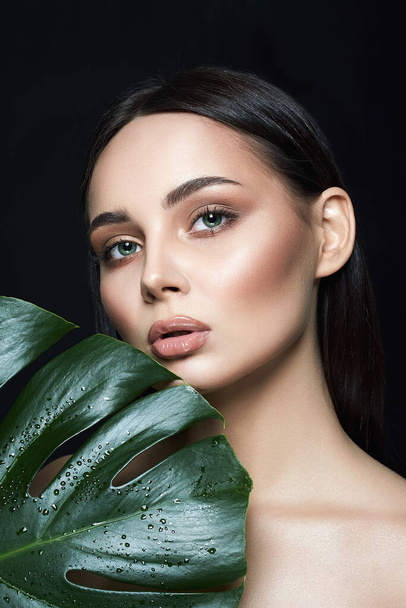 Beauty Portret van brunette meisje in palmbladeren. Mooie jonge vrouw met make-up. Natuurlijke cosmetica concept - Foto, afbeelding